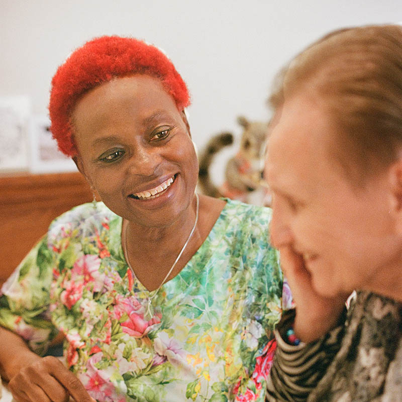 A red-haired woman sitting at a table and smiling with an elderly woman.